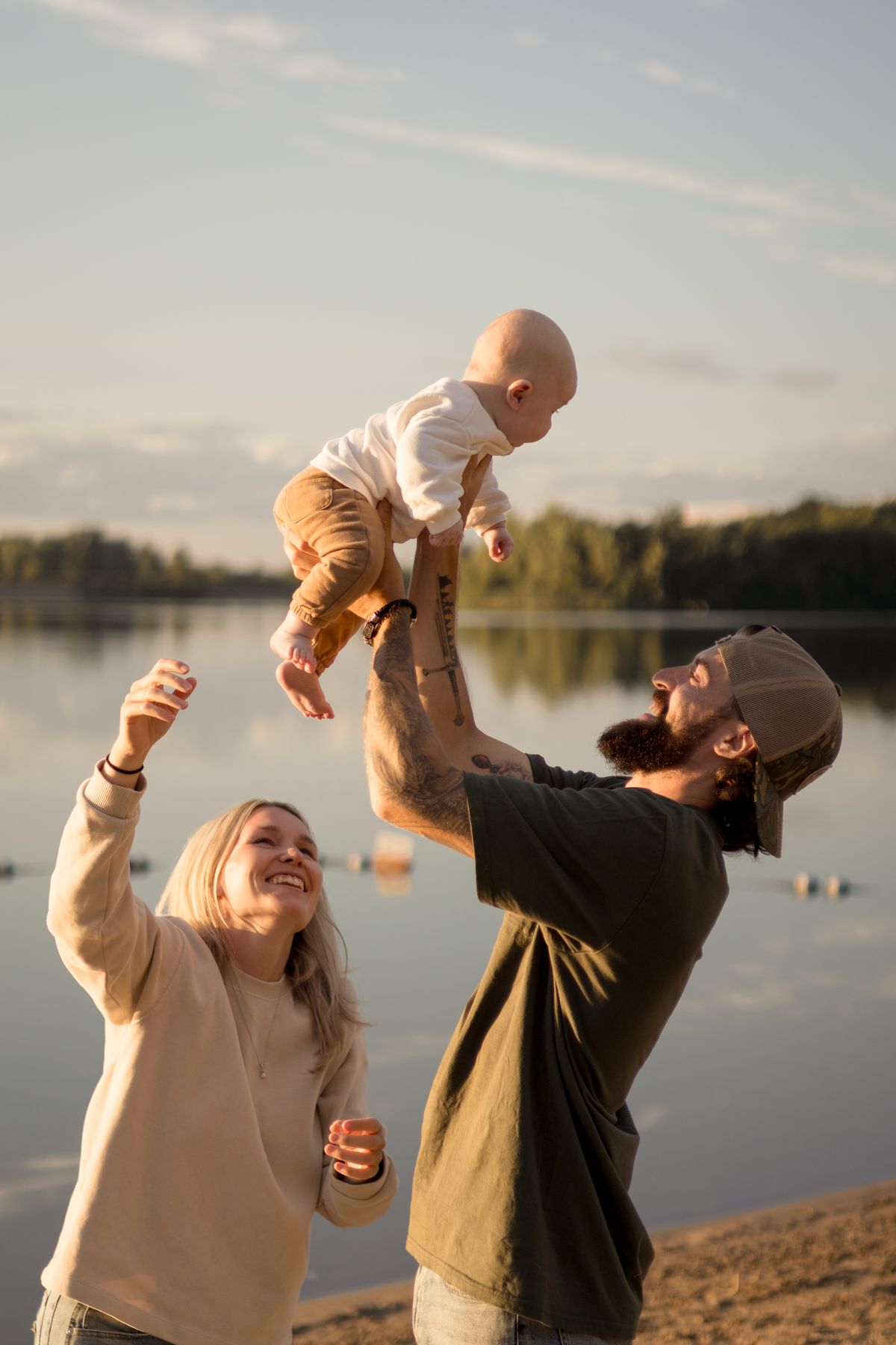 Parents soulevant joyeusement leur bébé au bord du lac au coucher du soleil