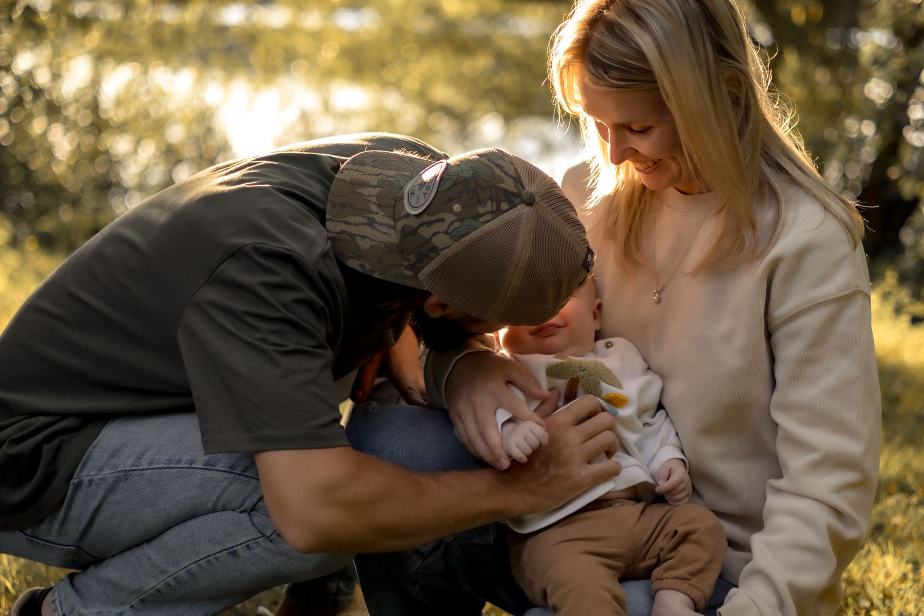 Parents embrassant tendrement leur bébé assis entre eux dans la verdure