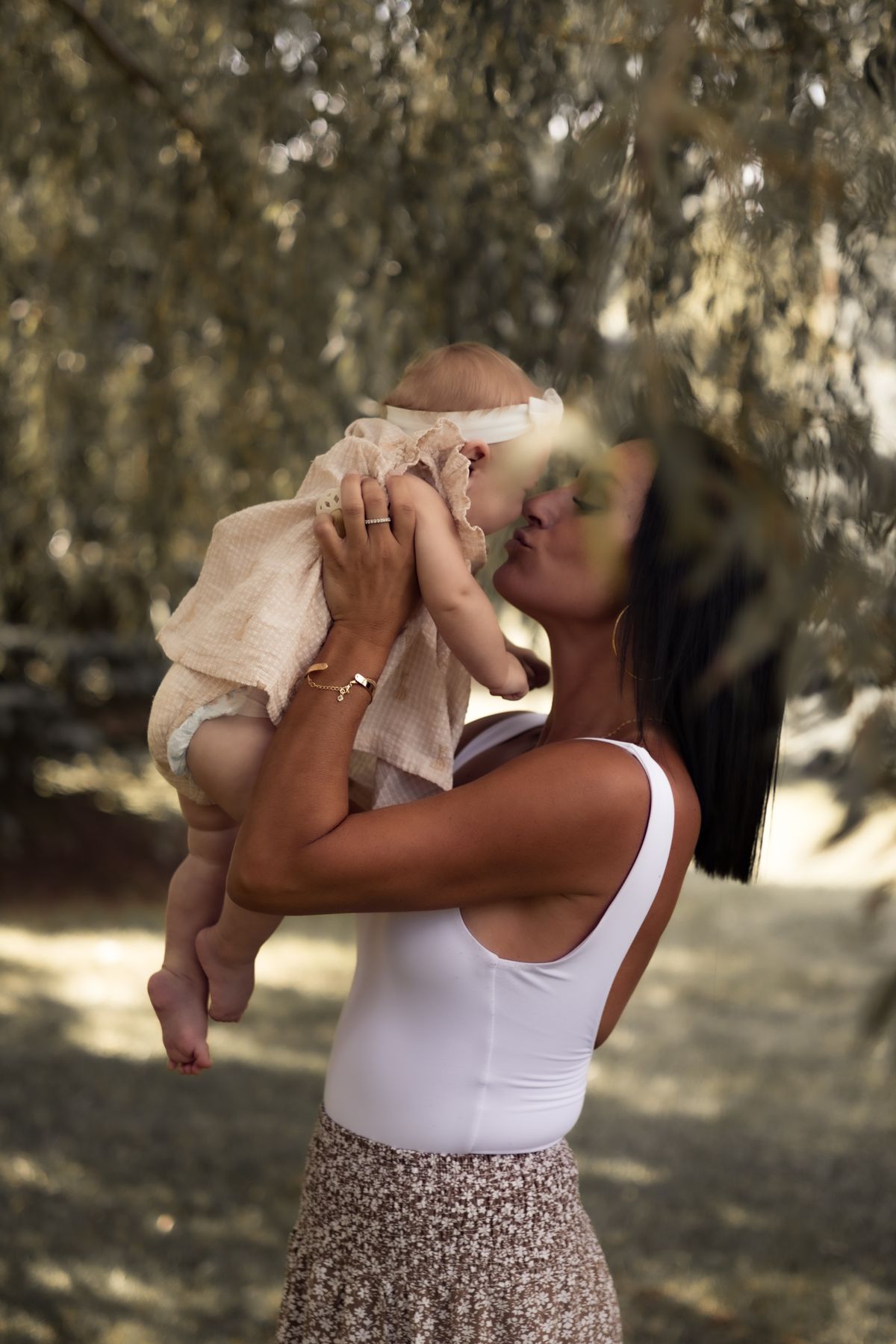 Mère soulevant son bébé sous les branches d'un saule