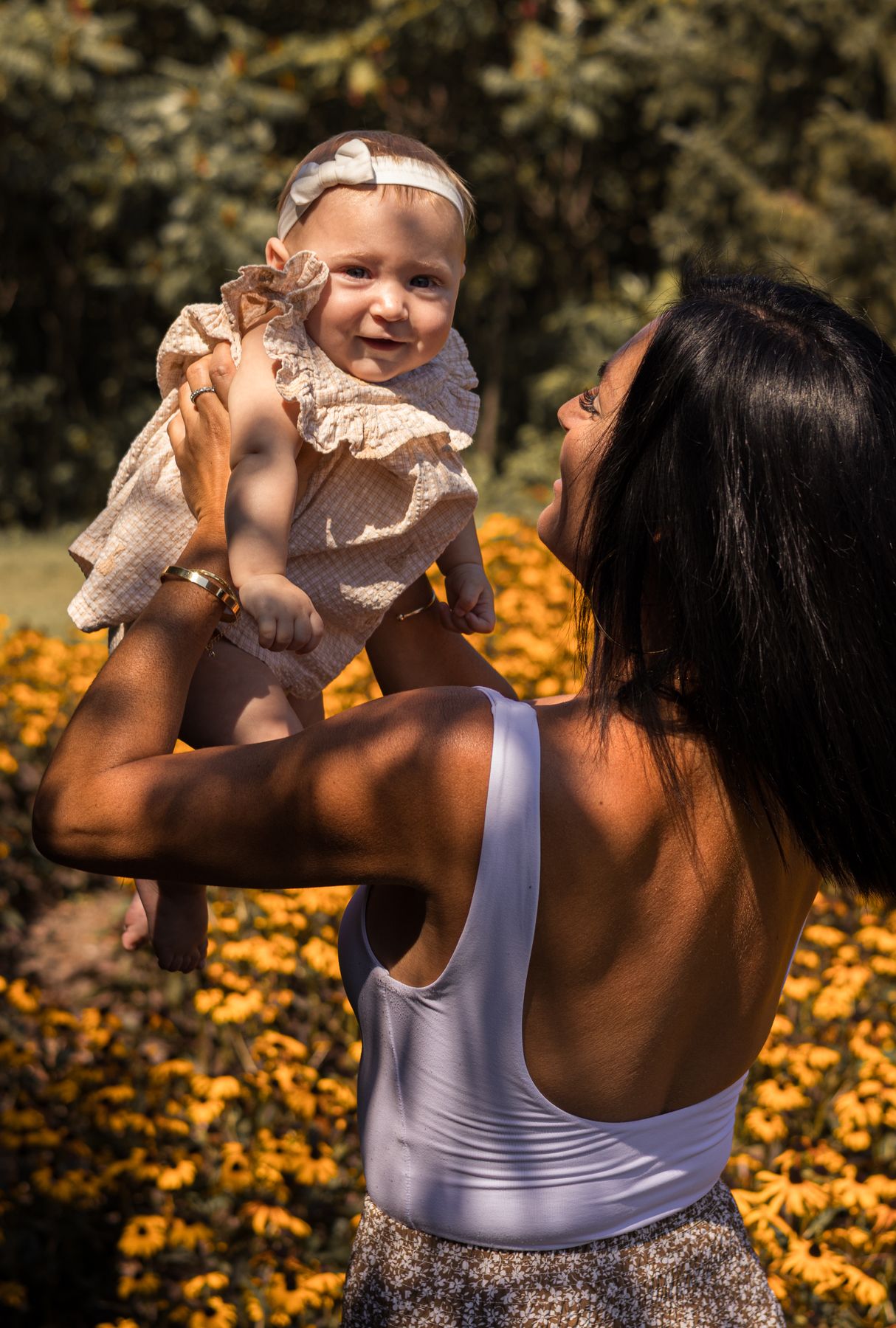 Bébé rieur porté à bout de bras dans un champ de fleurs jaunes