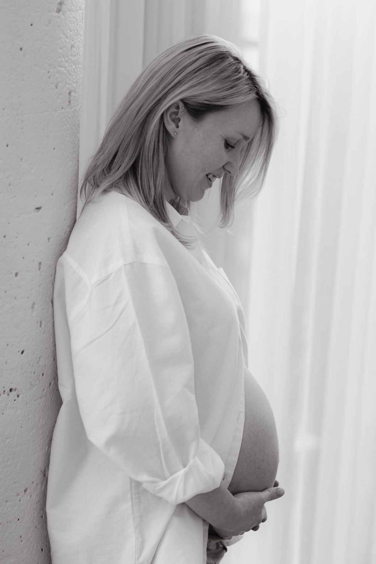 Future maman de profil dans une lumière douce, chemise blanche ouverte sur son ventre