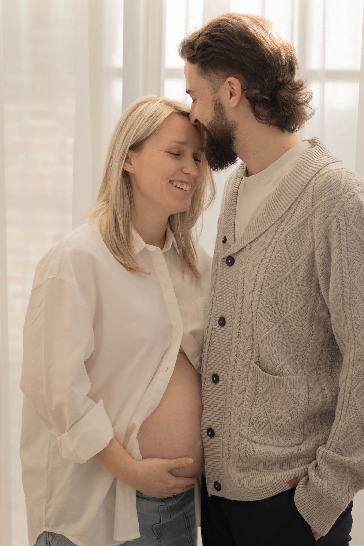 Couple enlacé près de la fenêtre, main posée sur le ventre rond